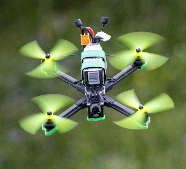 FPV-Copter mit Carbonrahmen und grünen Propellern im Flug.